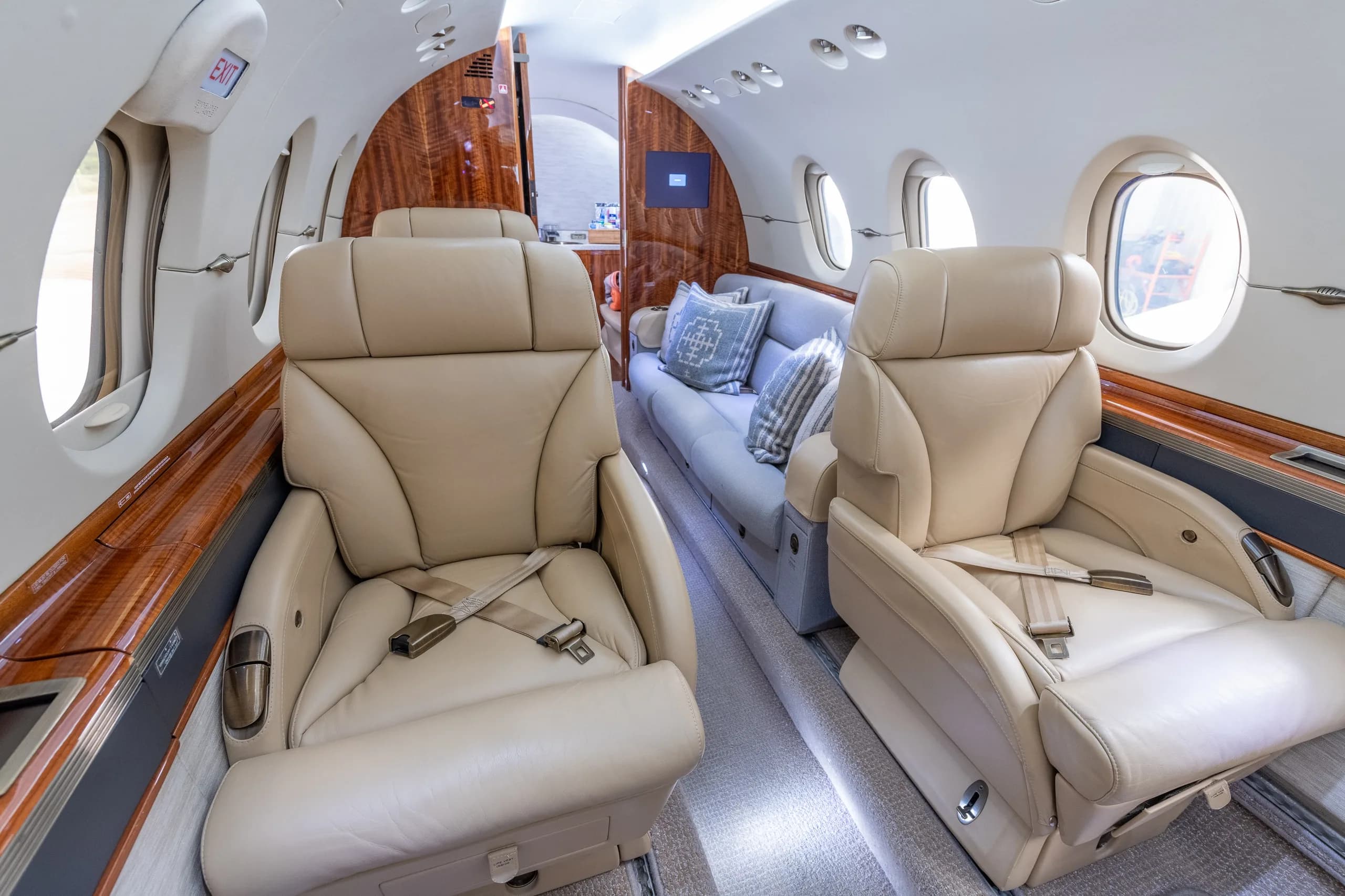 A view of the aircraft cabin showing two beige leather seats in the foreground and a light grey couch further back.