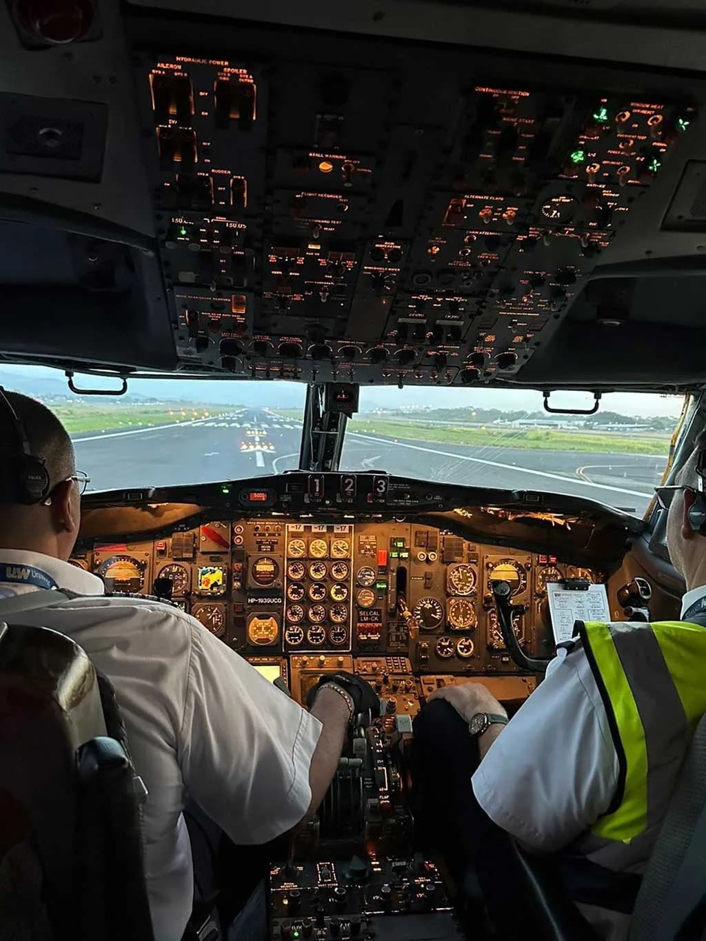 Two pilots in the cockpit of a Boeing 727, with illuminated instruments and a view of the runway ahead.