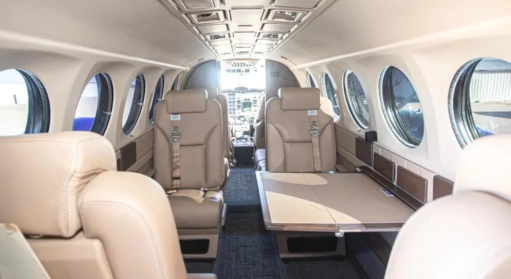 The beige leather interior of an aircraft cabin with a fold-out table and the cockpit visible in the distance.