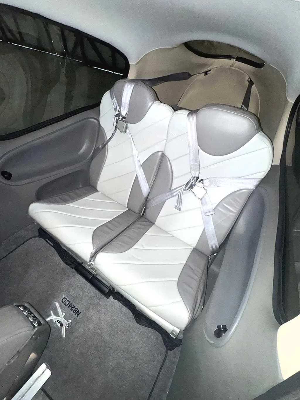 The rear cabin seats of a Cirrus SR20 aircraft, featuring gray and white leather upholstery and seatbelts, with the aircraft's registration N824CD visible on the floor mat.