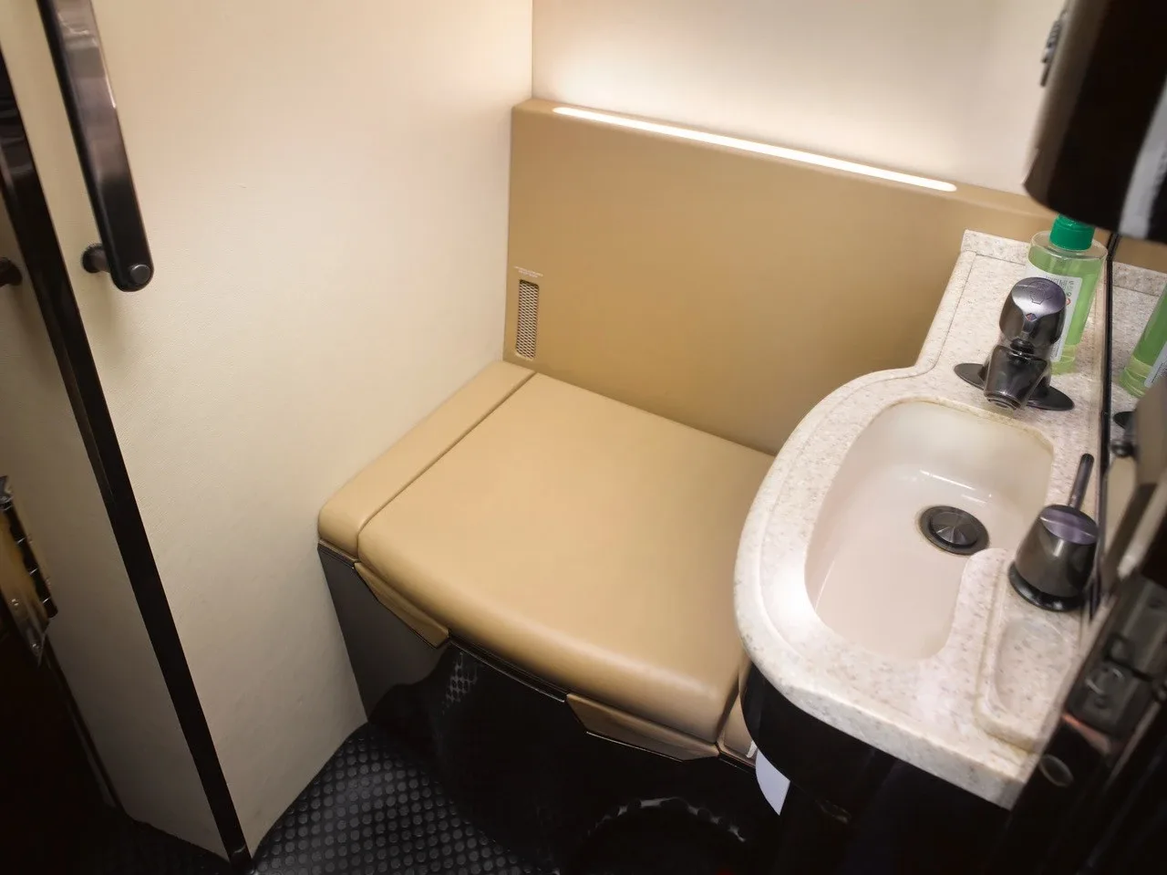 A small aircraft lavatory with a sink and a beige bench seat.