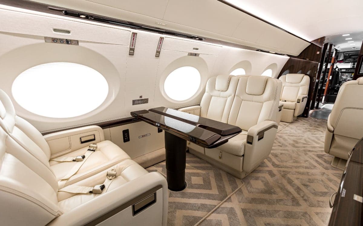 A view of the Gulfstream G500 cabin featuring cream-colored leather seats and a dark wood table.