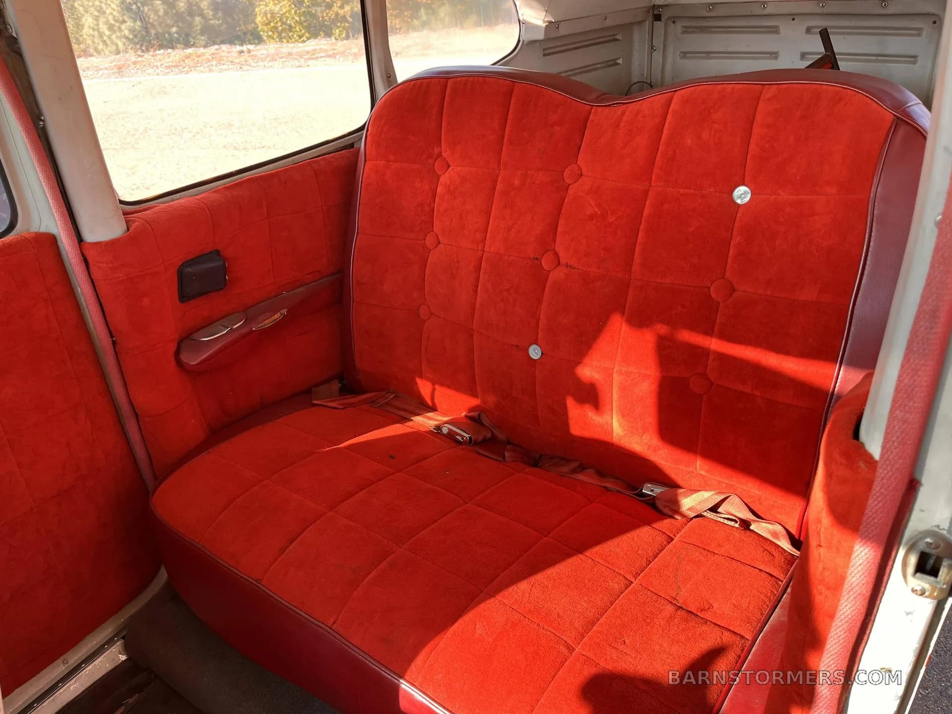 The red upholstered rear bench seat of a Cessna 182 aircraft cabin.