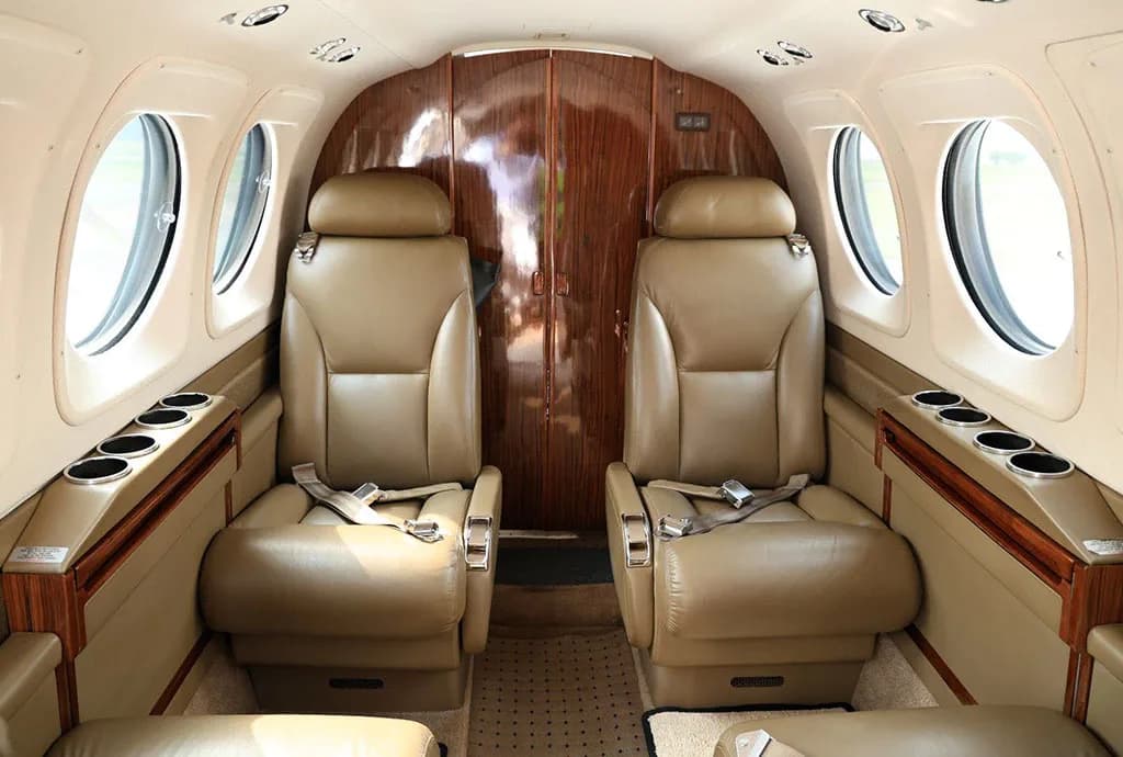 The interior cabin of an aircraft, featuring two tan leather seats and a wooden partition at the front.