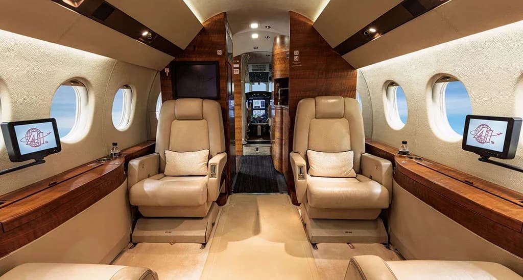 The forward section of a business jet's cabin, featuring two large beige leather seats and wood paneling.
