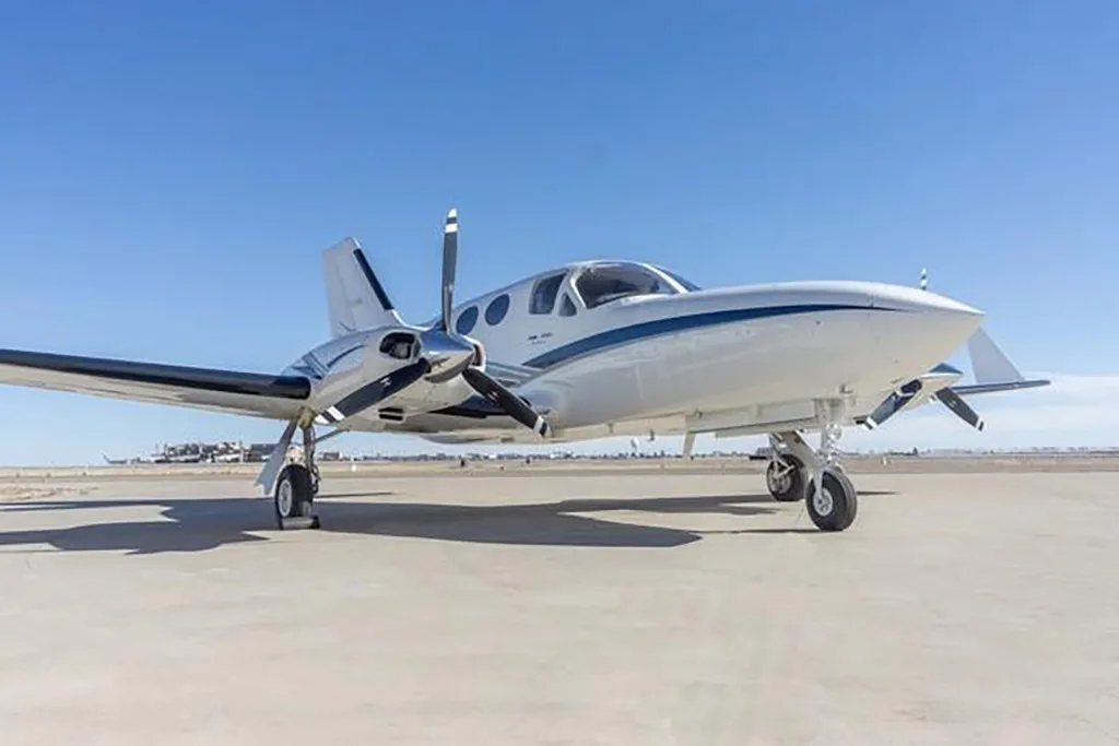 A low-angle view of a white twin-engine Cessna 414 Chancellor aircraft with blue stripes on an airfield.
