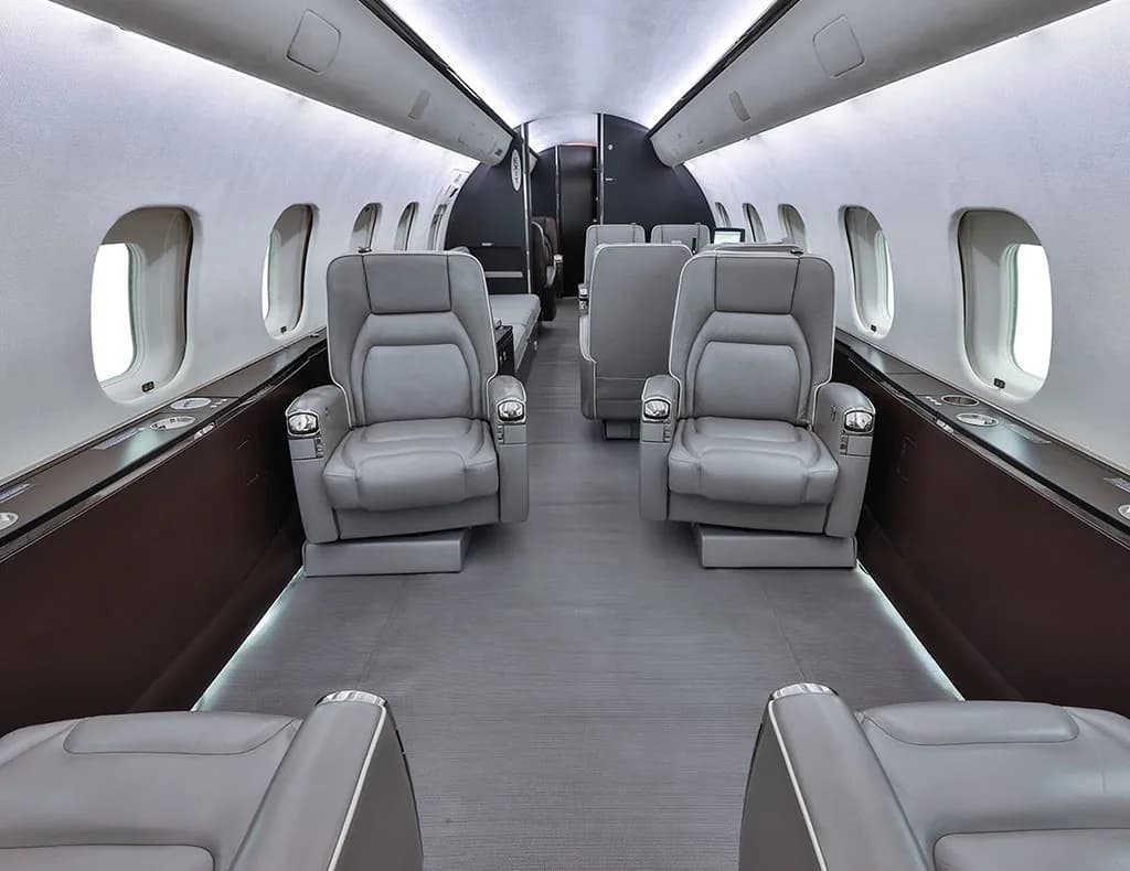 The interior cabin of a private jet with grey leather seats and dark brown side panels.