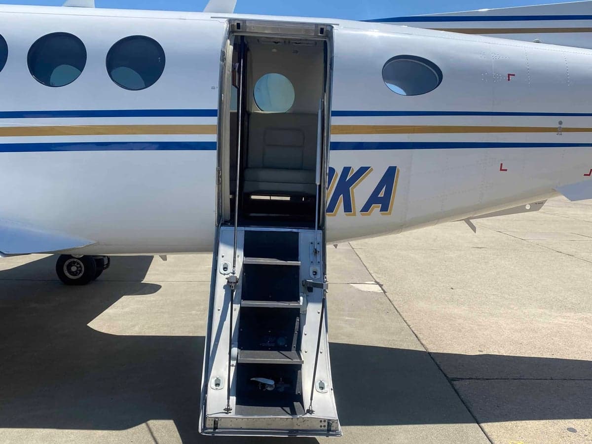 The open airstair door of the white and blue Beechcraft King Air 350, showing steps leading into the cabin.