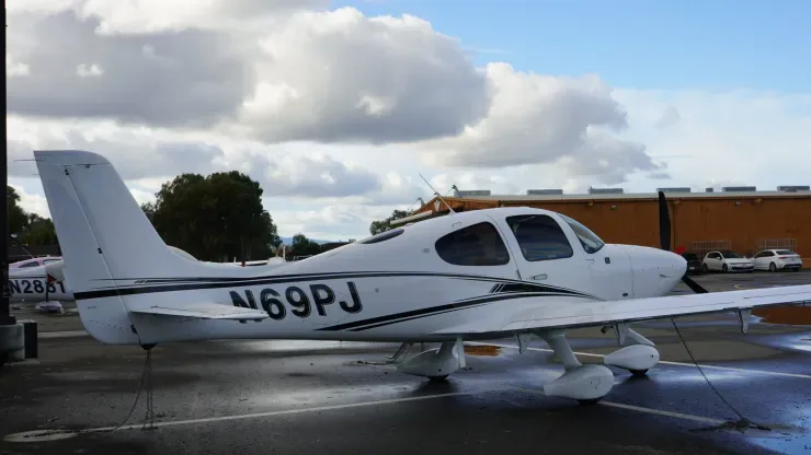 A Cirrus aircraft with registration N69PJ parked on the tarmac with a cloudy sky.