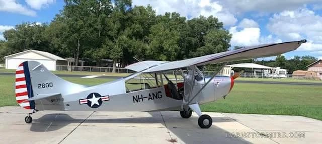 A silver Aeronca L-16 Liaison aircraft with "Weekend Warrior" nose art and US Air National Guard markings, parked on a concrete pad.