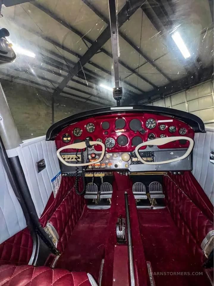 A vintage-style cockpit with a red instrument panel, white yokes, and red quilted interior.