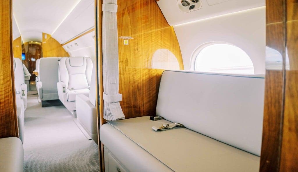 The aircraft's interior features a wood table and white leather seats.