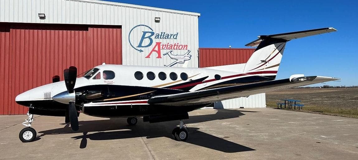 Side view of a Beechcraft King Air parked on the tarmac in front of a hangar.