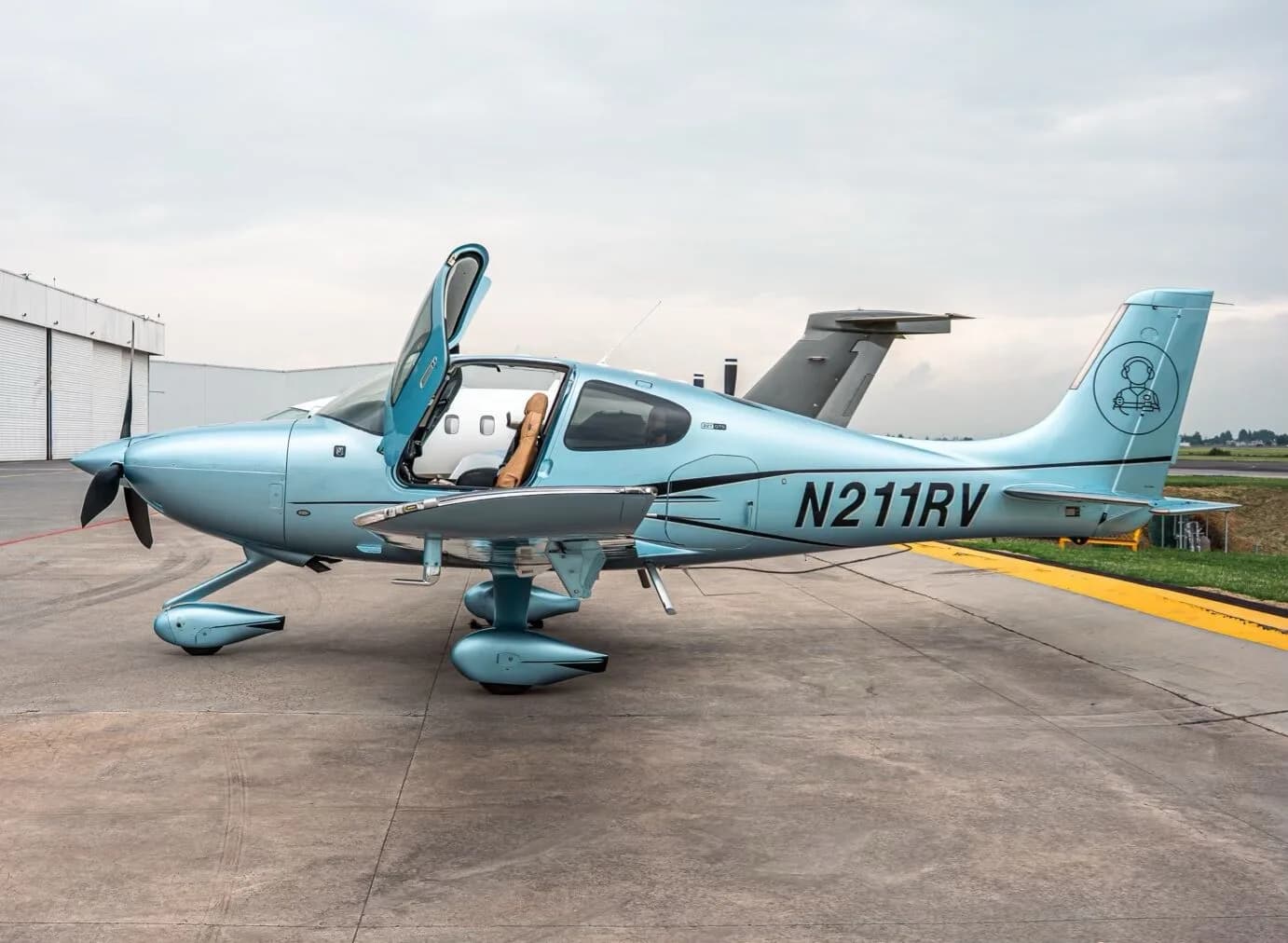 A light blue Cirrus SR22T aircraft with registration N211RV parked on an airfield, showing the right side with the door open.