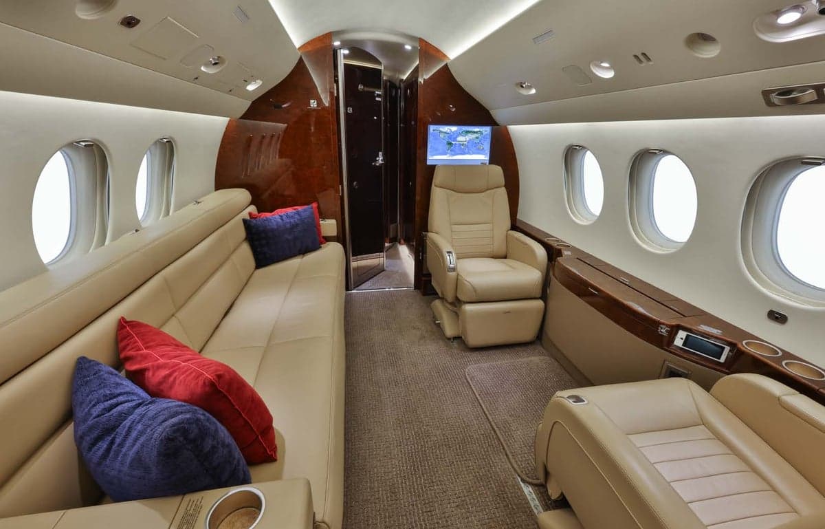 The aircraft's interior features a tan leather couch and a single seat with a monitor.