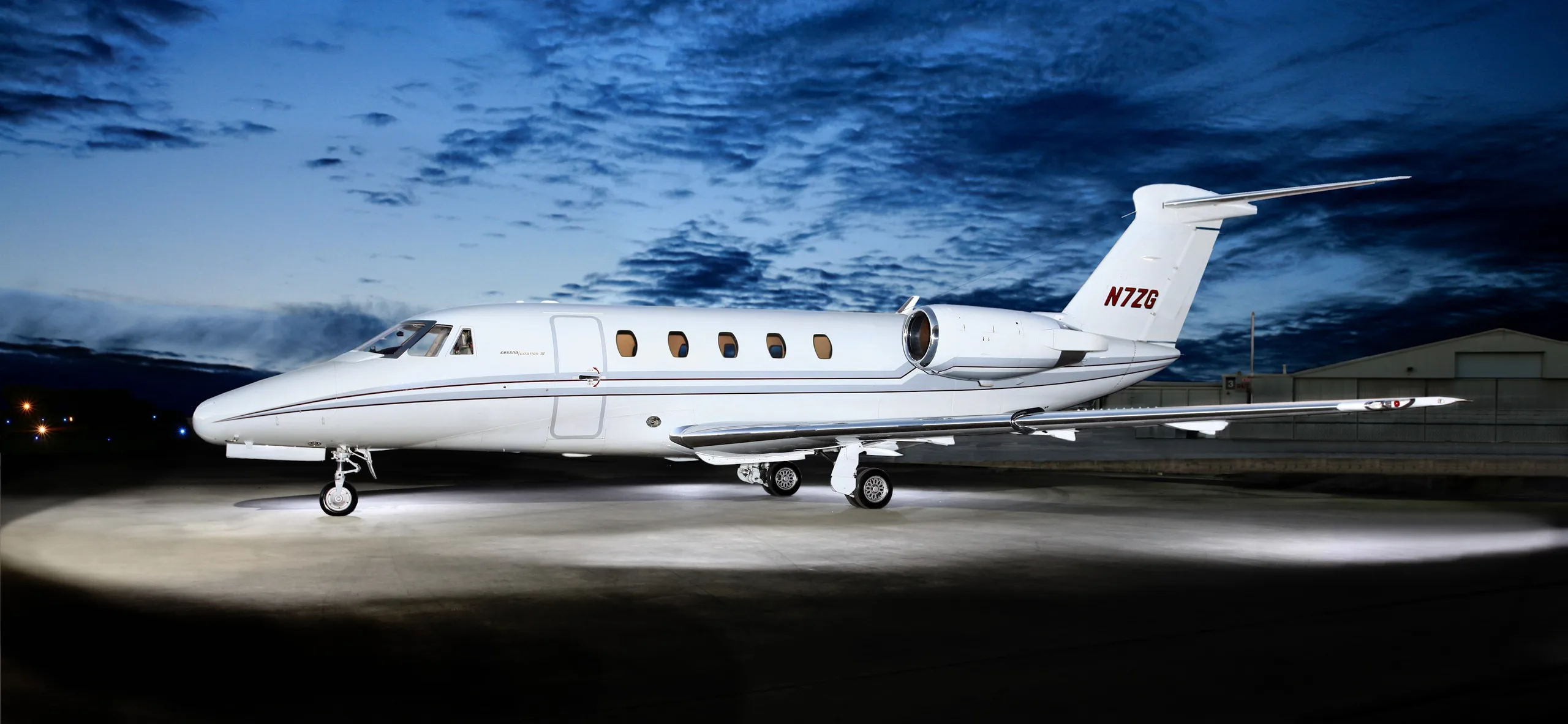A white Cessna Citation II business jet with a dark stripe and tail number N7ZG is parked on a tarmac at night.