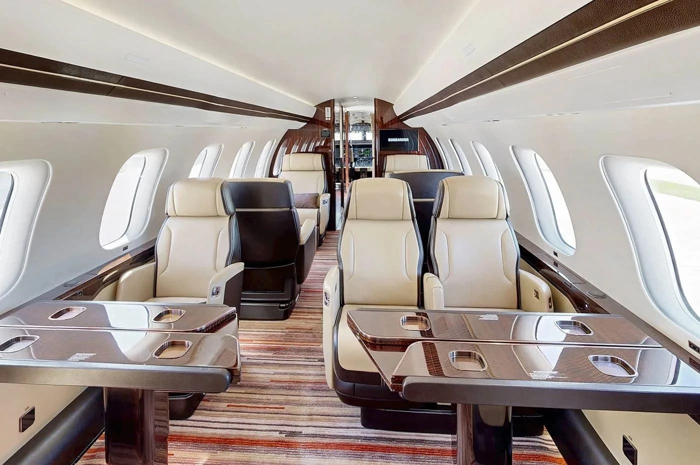 The luxurious cabin interior of a Bombardier Global business jet, featuring beige leather seats and dark wood tables.