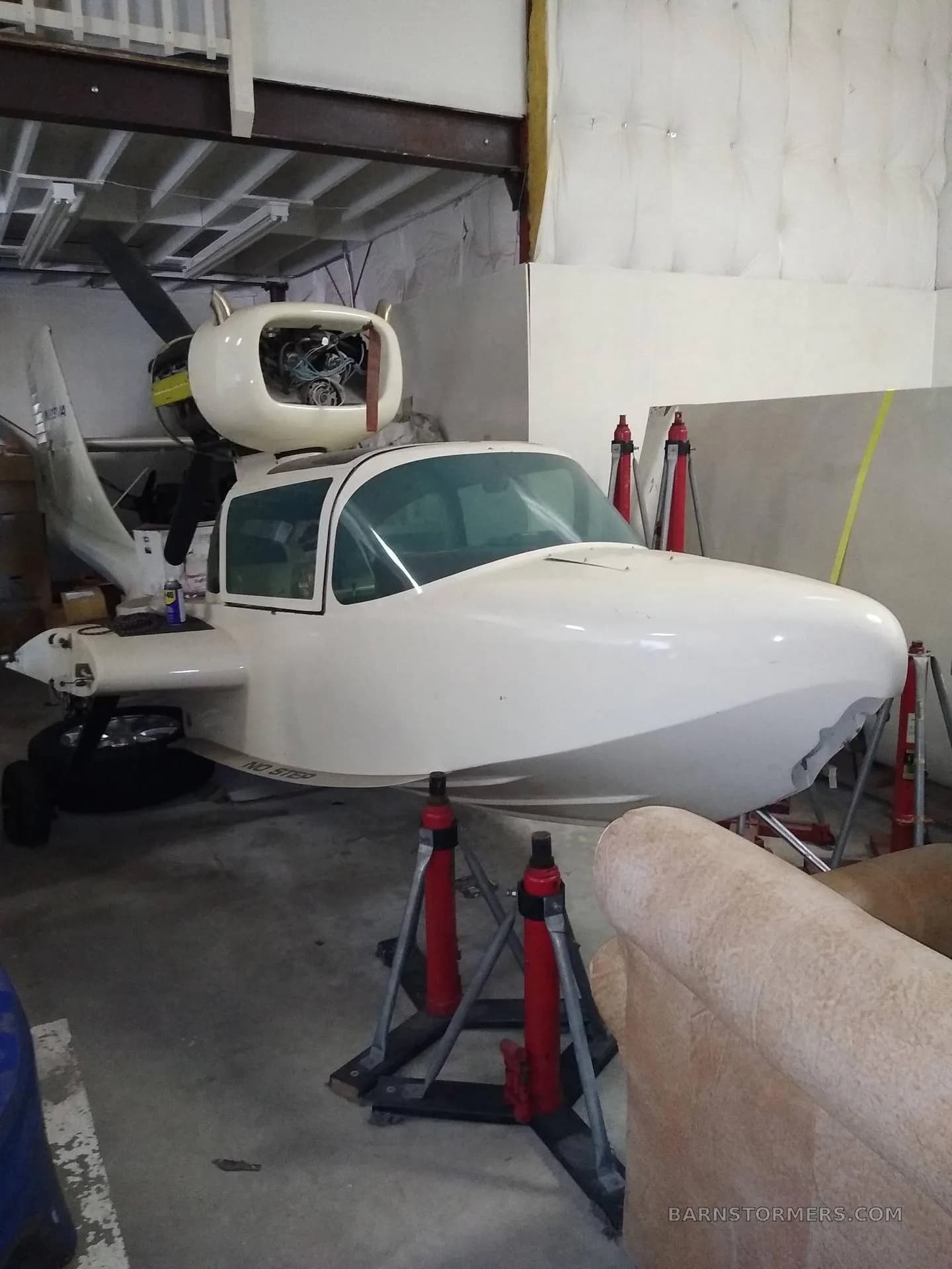 A white aircraft, partially disassembled and supported by red jacks, sits inside a hangar.