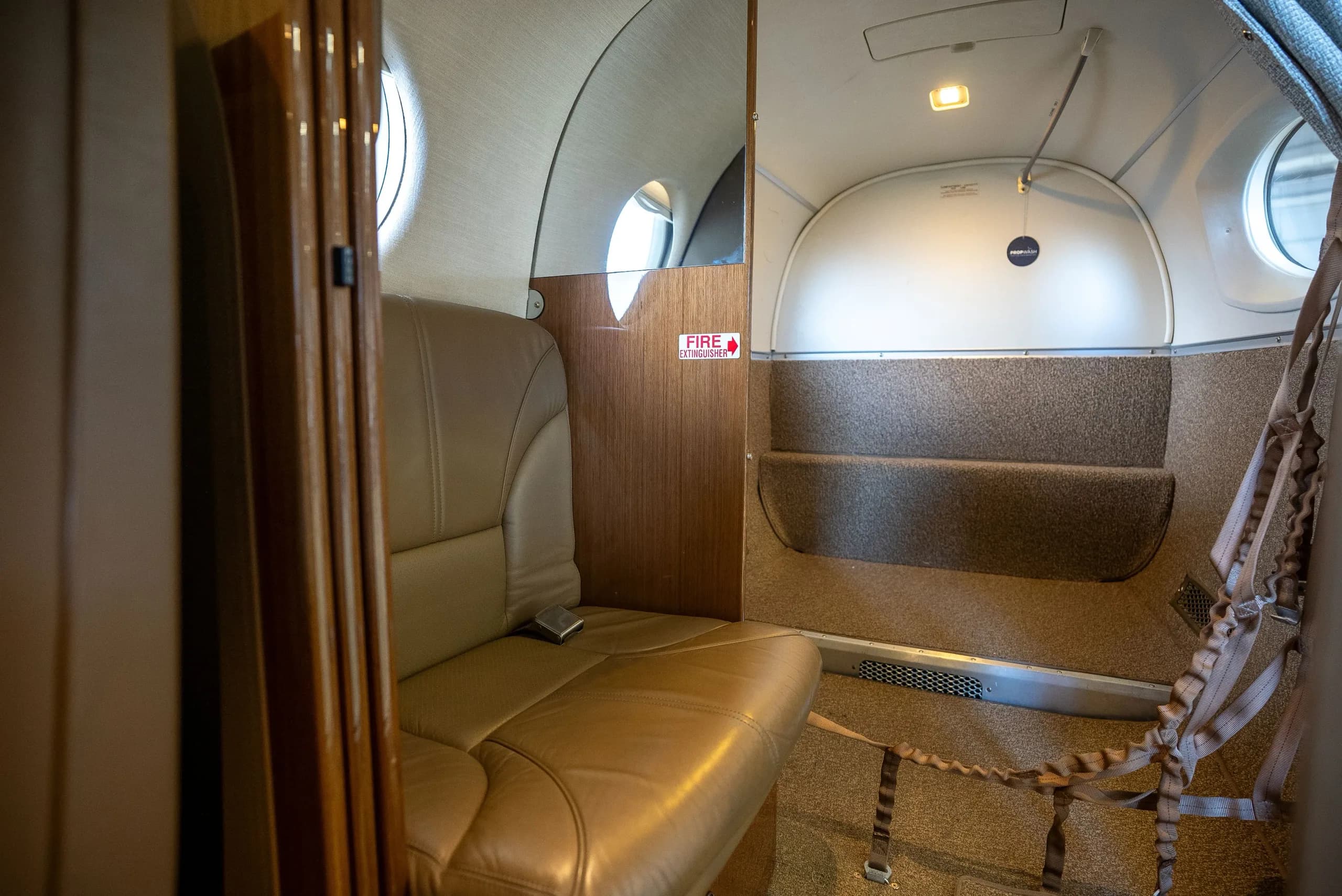 The rear cabin interior of an aircraft, showing a tan leather side-facing seat and a cargo net.