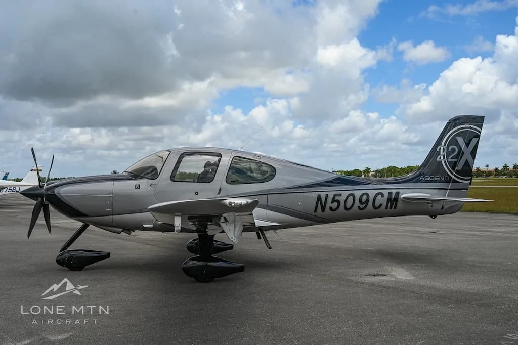 A silver and black Cirrus SR22 aircraft with registration N509CM parked on an airfield, viewed from the left side.