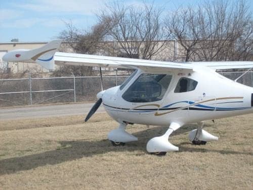 A white light sport aircraft is parked on a grassy field.