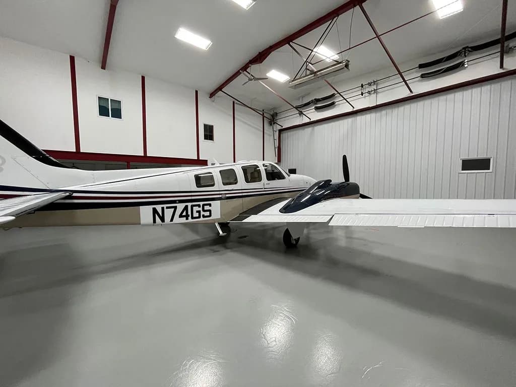 A side view of the white and tan twin-engine aircraft N74GS with dark blue and red stripes, parked in a hangar.