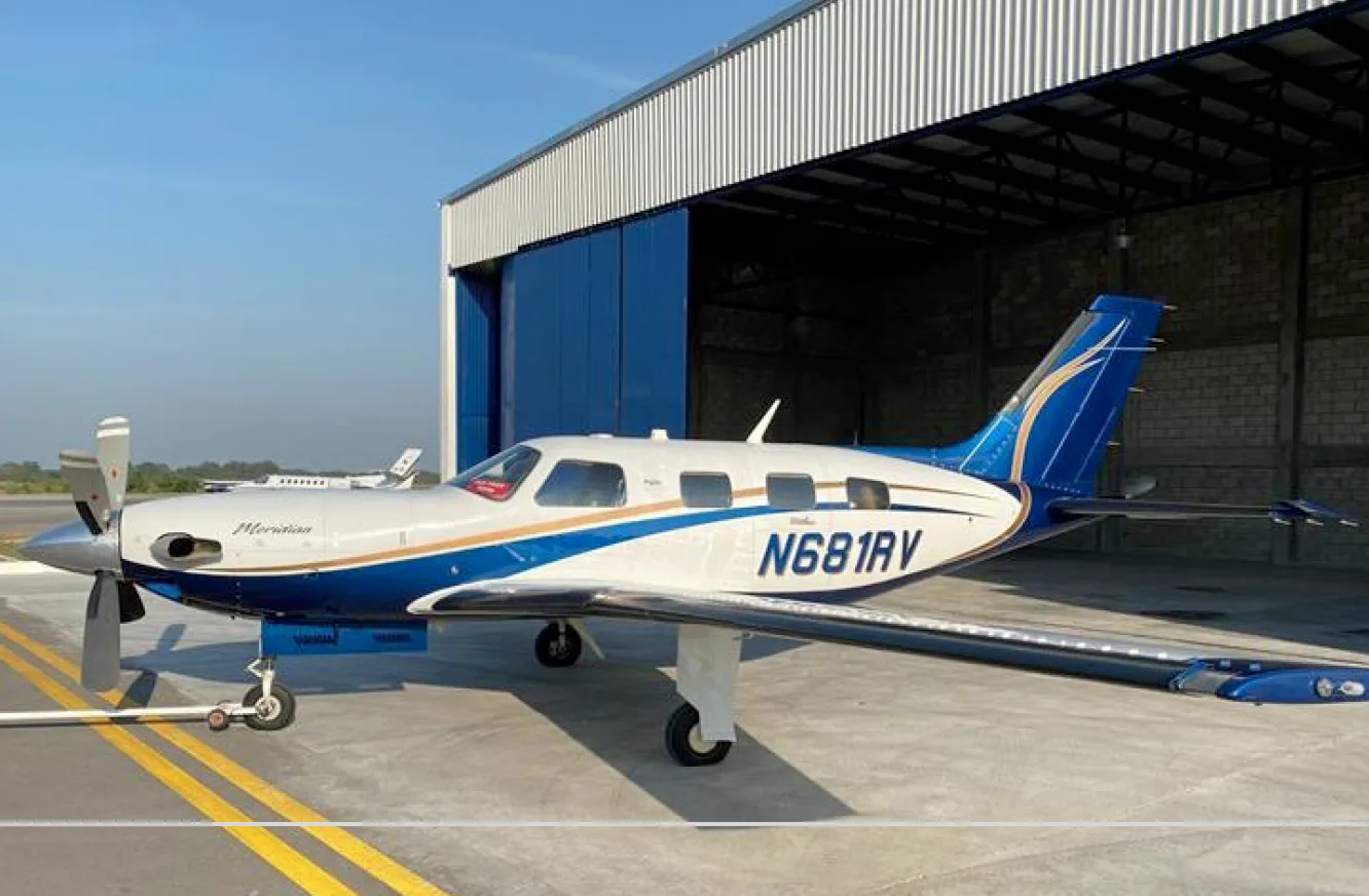 A Piper Meridian aircraft is parked in front of a hangar.