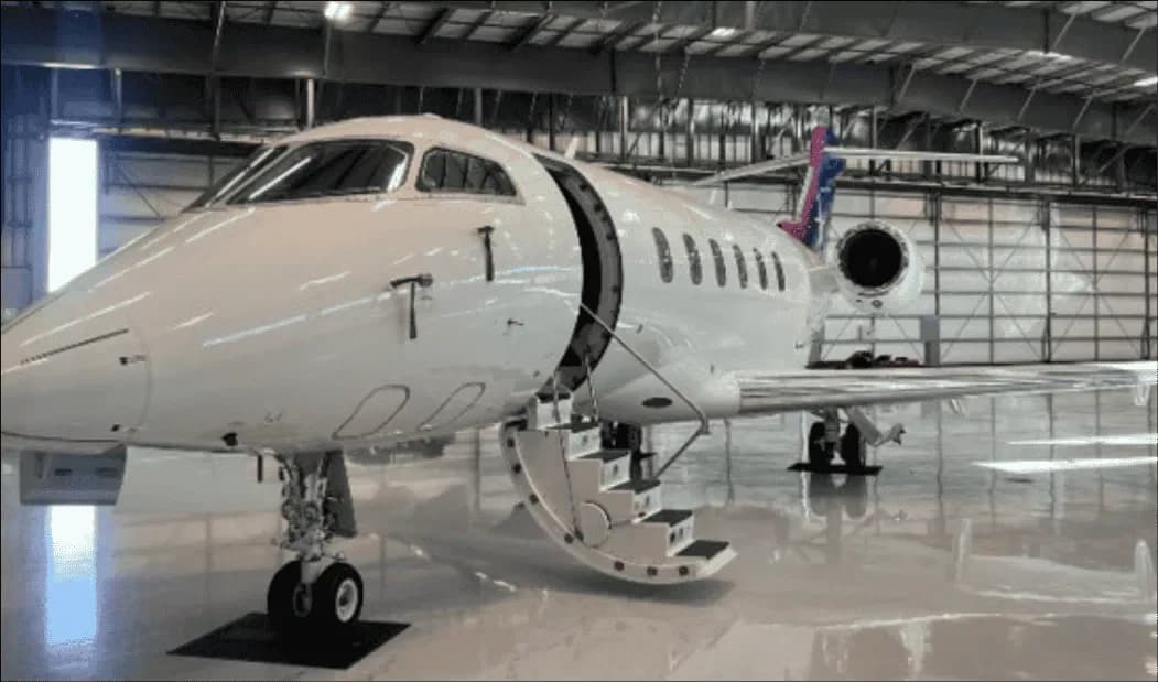 A white business jet with its main entry door open and stairs extended, parked inside a large hangar.