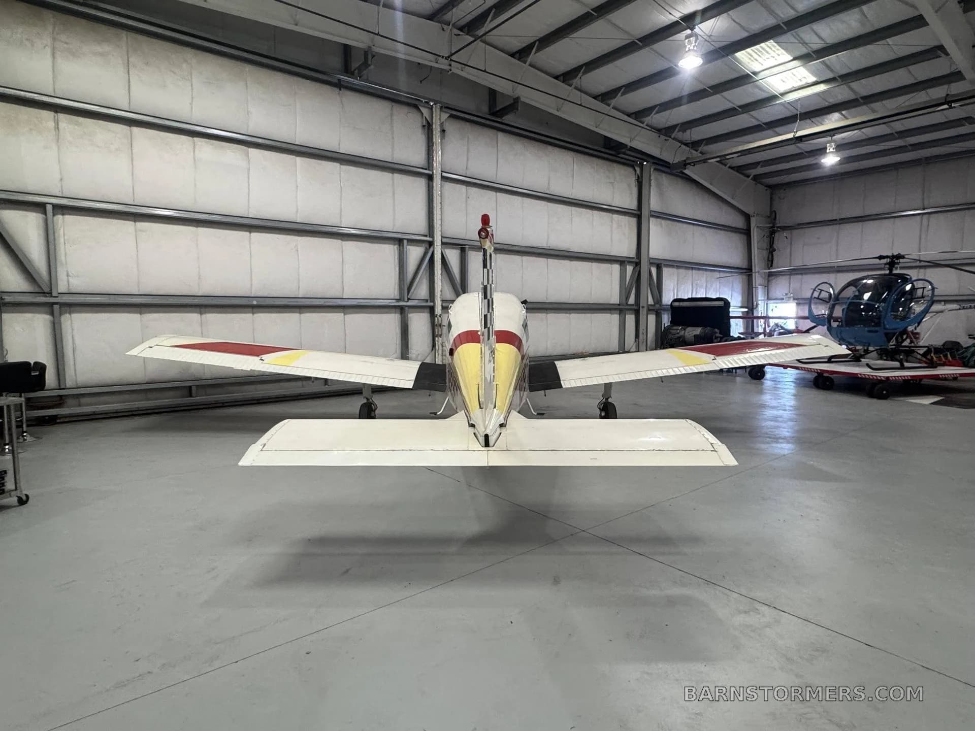 The rear view of a white and red Beechcraft Sundowner N229FC with a checkered tail, parked in a hangar.