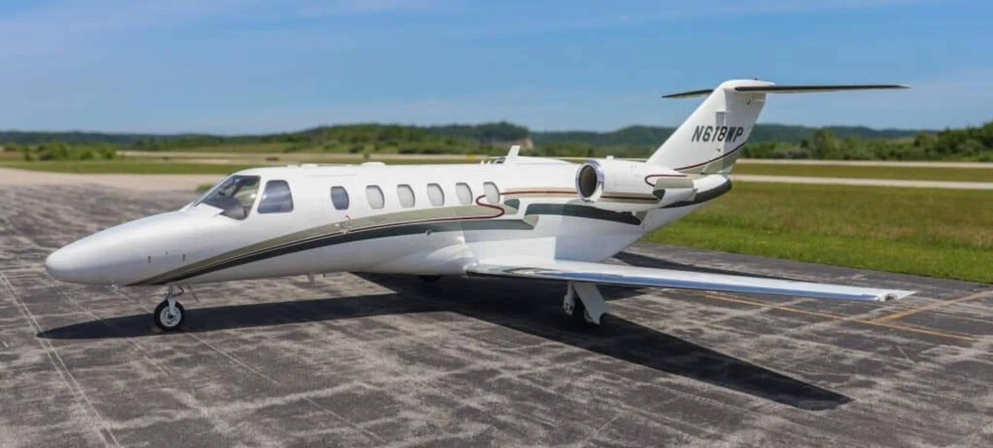 A white Cessna Citation CJ2+ business jet with green and red stripes parked on an airfield.