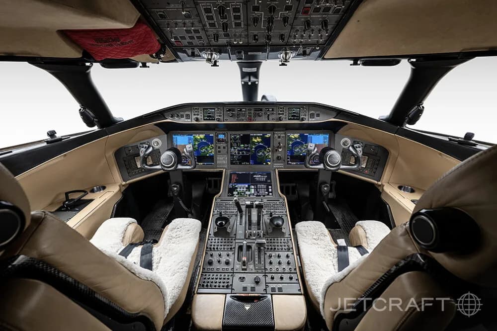 The modern cockpit of a Bombardier Global business jet, featuring multiple digital displays and tan leather seats.