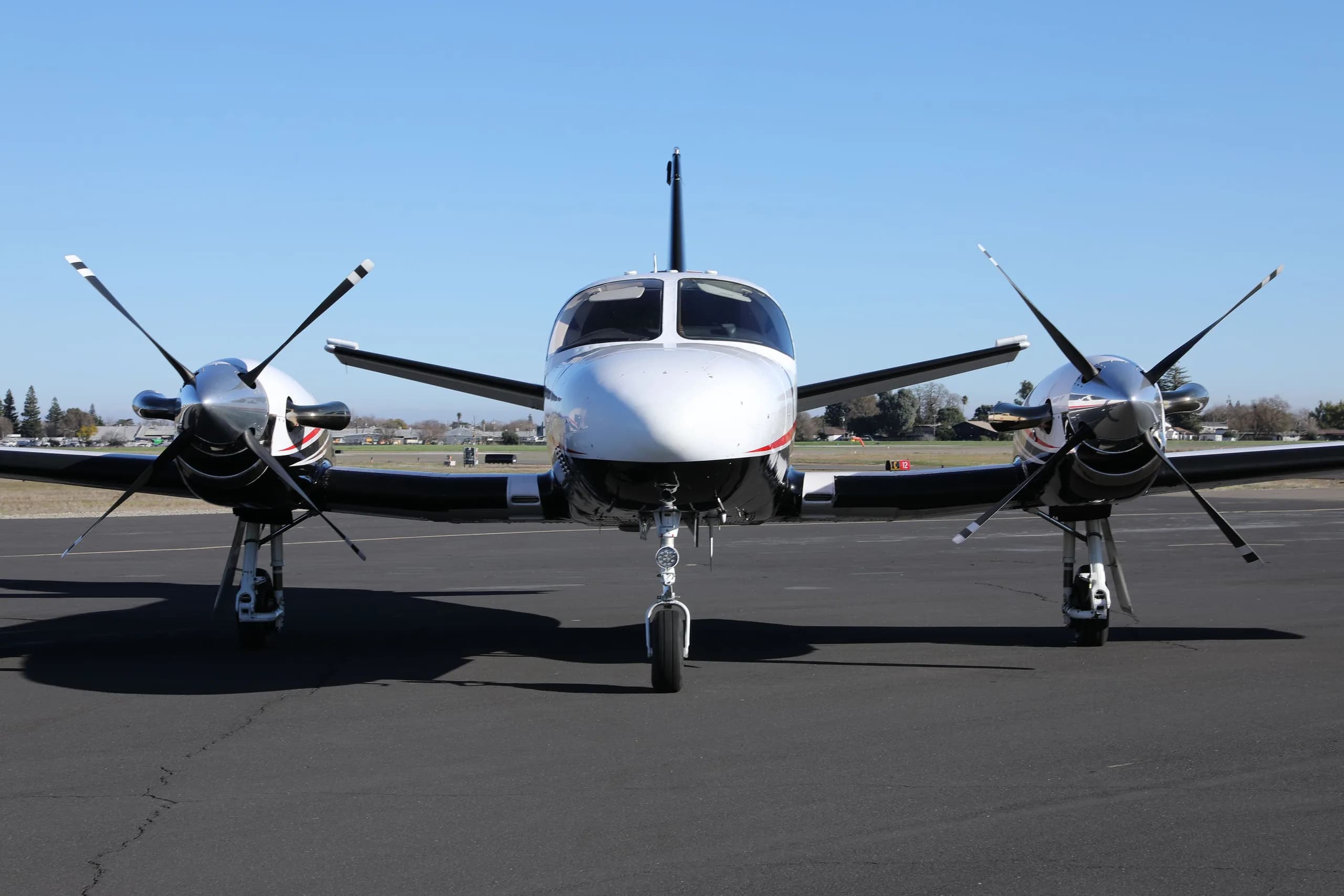 A head-on view of the white, black, and red Cessna 414 Chancellor parked on an asphalt tarmac.