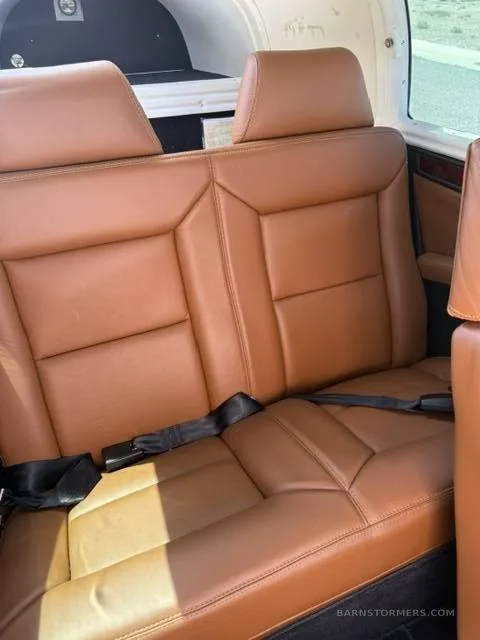 Two rows of tan leather aircraft seats with black seatbelts in the cabin of an aircraft.