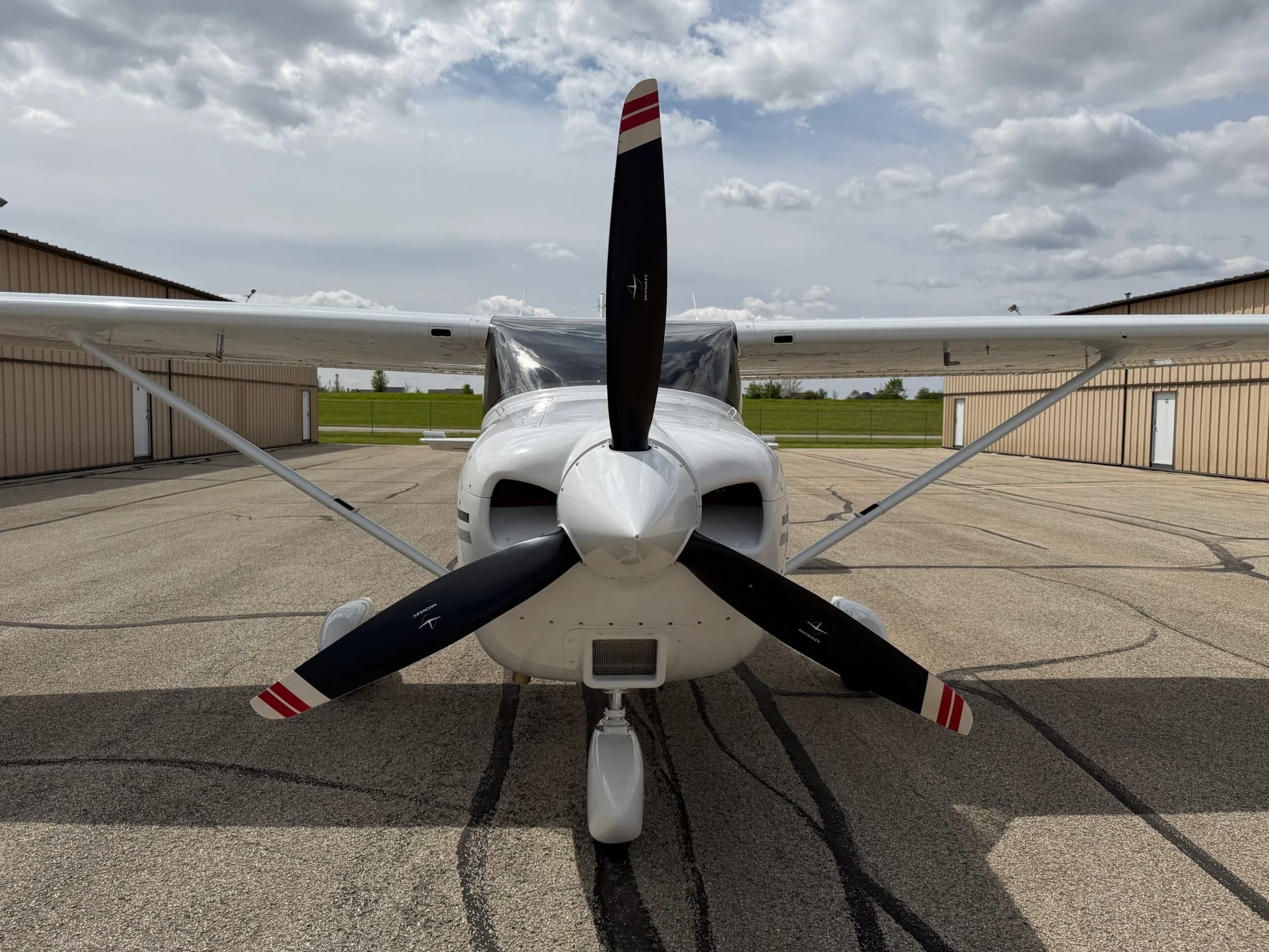 A full front view of the white single-engine aircraft with its propeller stopped, parked on the tarmac.