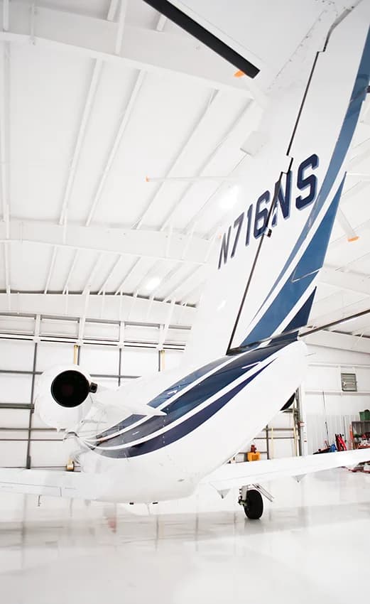 A close-up view of the tail of a white business jet (N716NS) with blue stripes in a hangar.