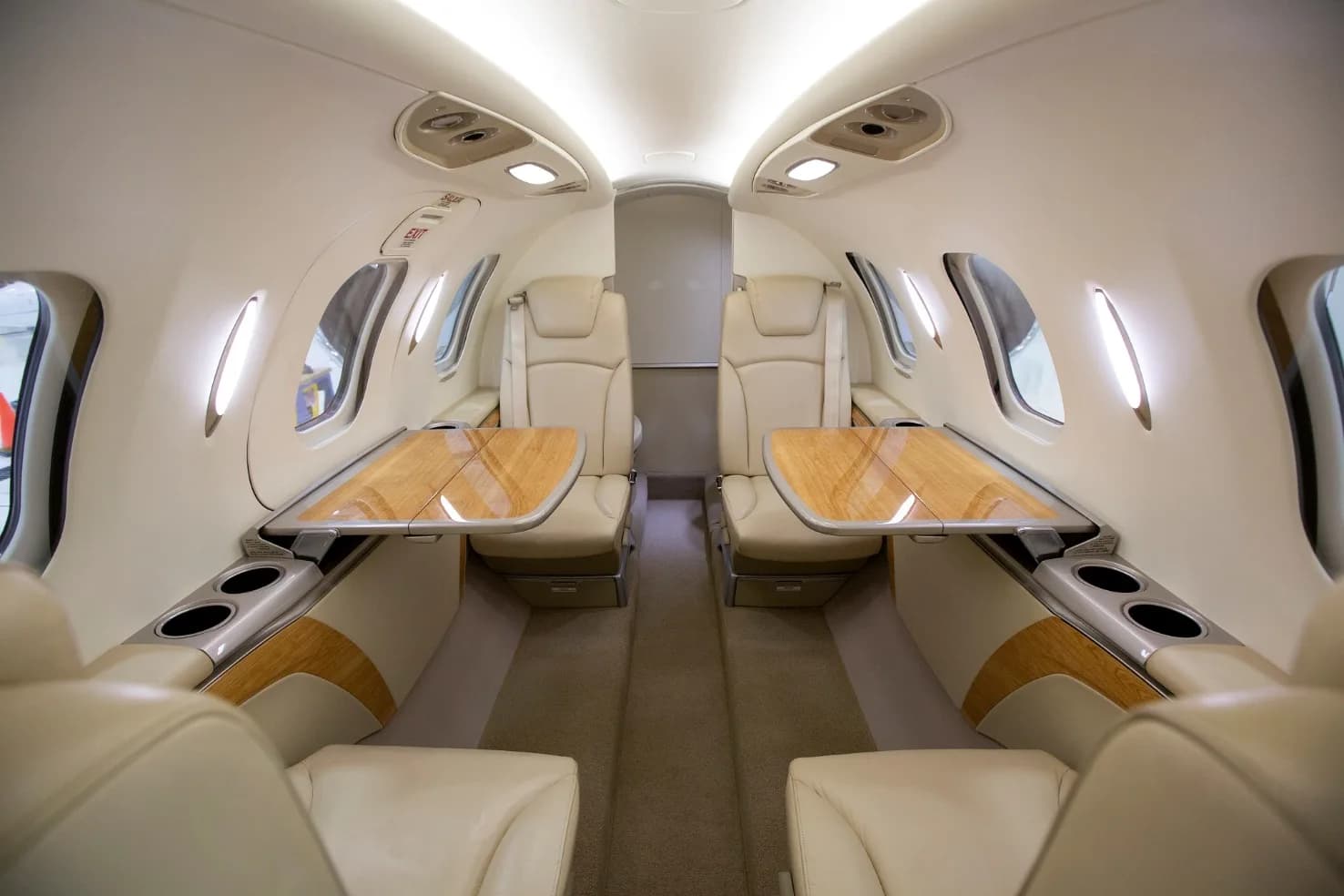 The aircraft's cabin interior with light-colored leather seats and two wooden fold-out tables extended.