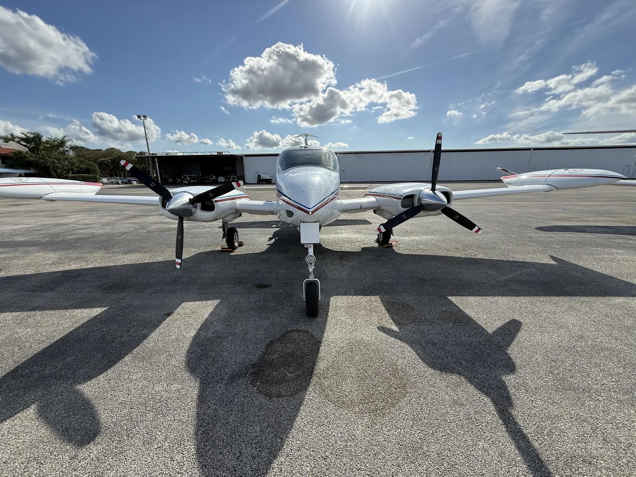 A front view of a white Cessna 310L with red and blue stripes parked on an airport tarmac.
