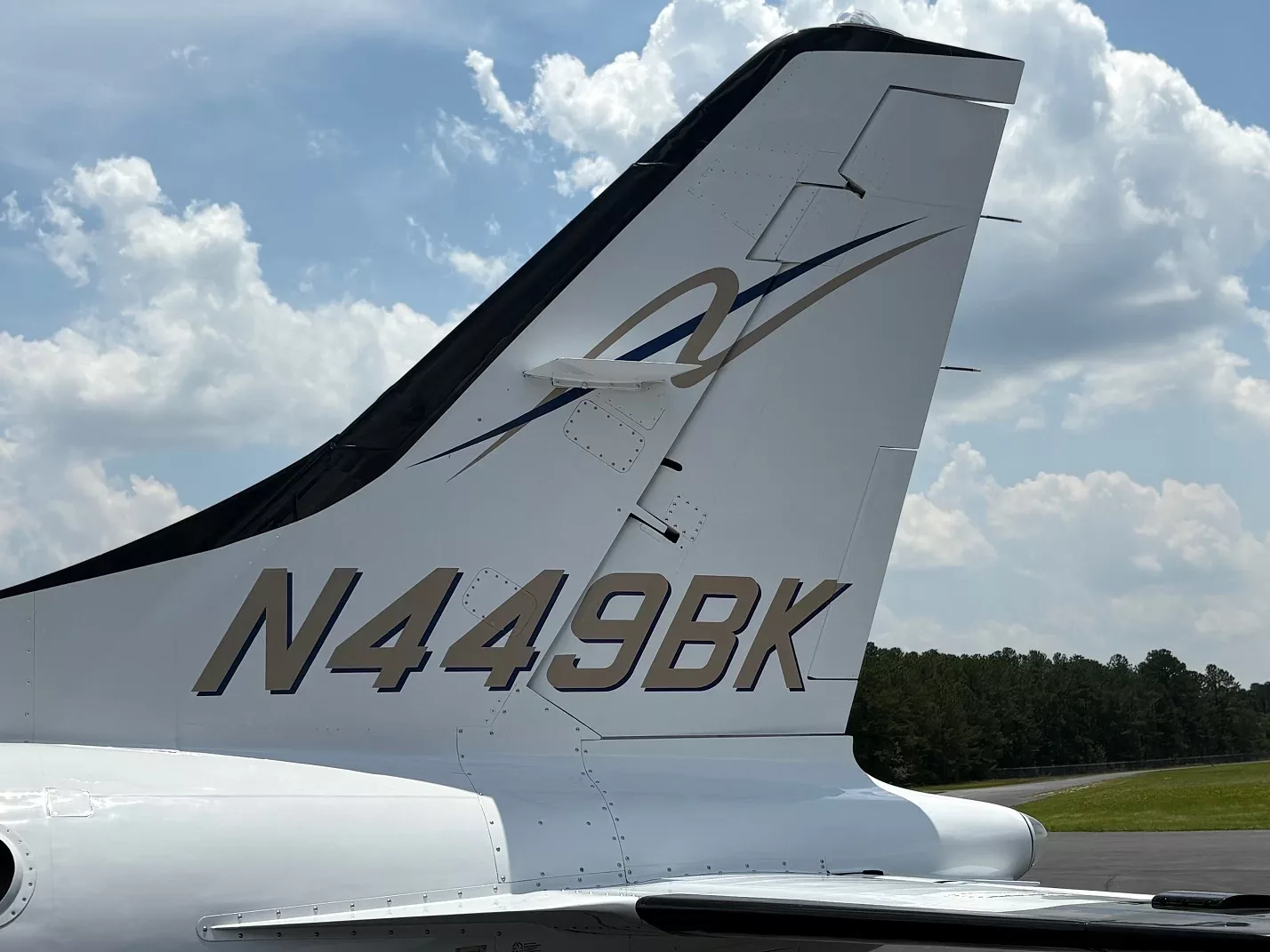 Close-up of the tail of a white aircraft showing the registration N449BK and a gold and blue stripe design.