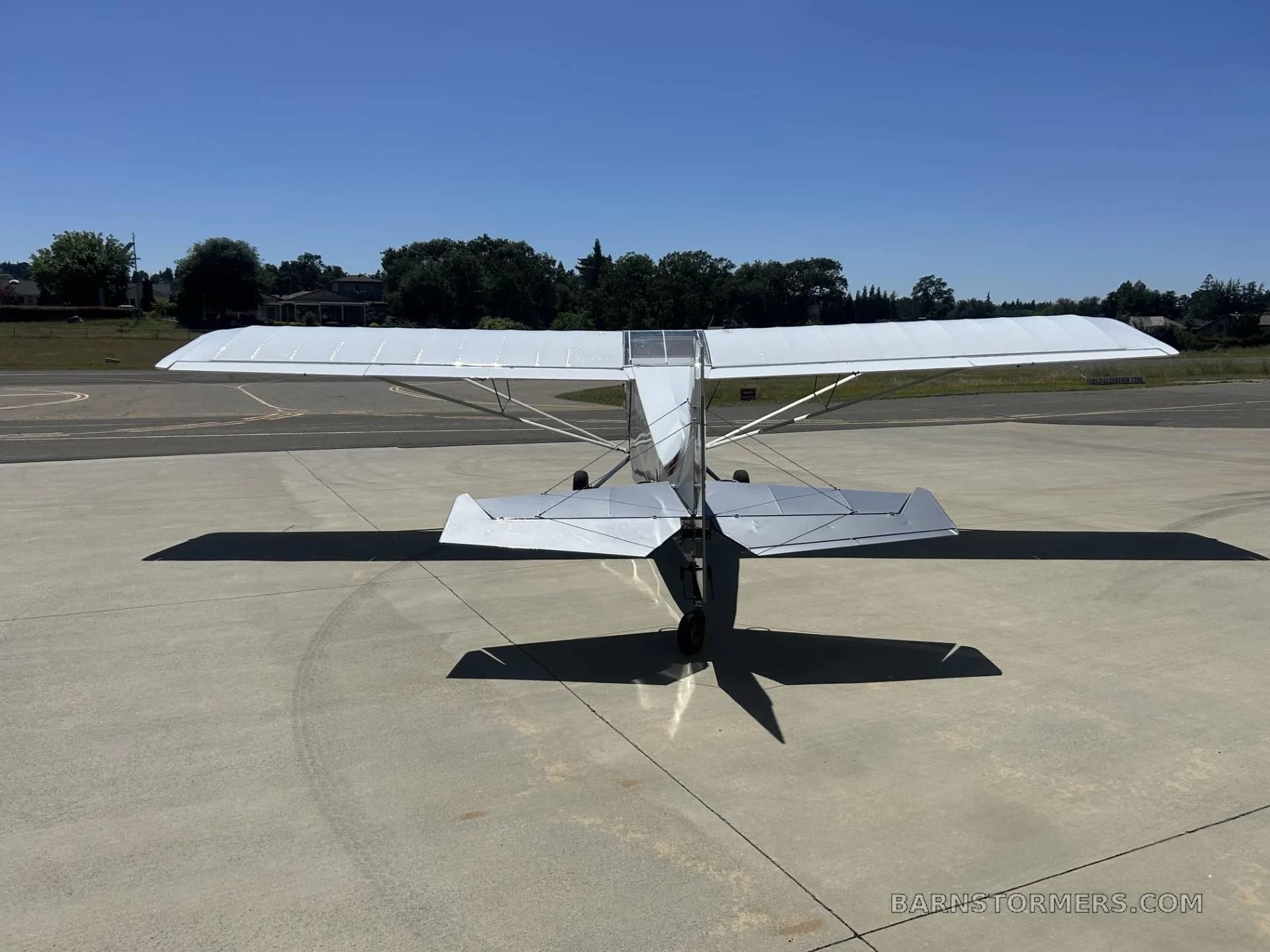 A rear view of a white and grey Rans S-21 Outbound aircraft parked on an airfield, showing its tail and wings.