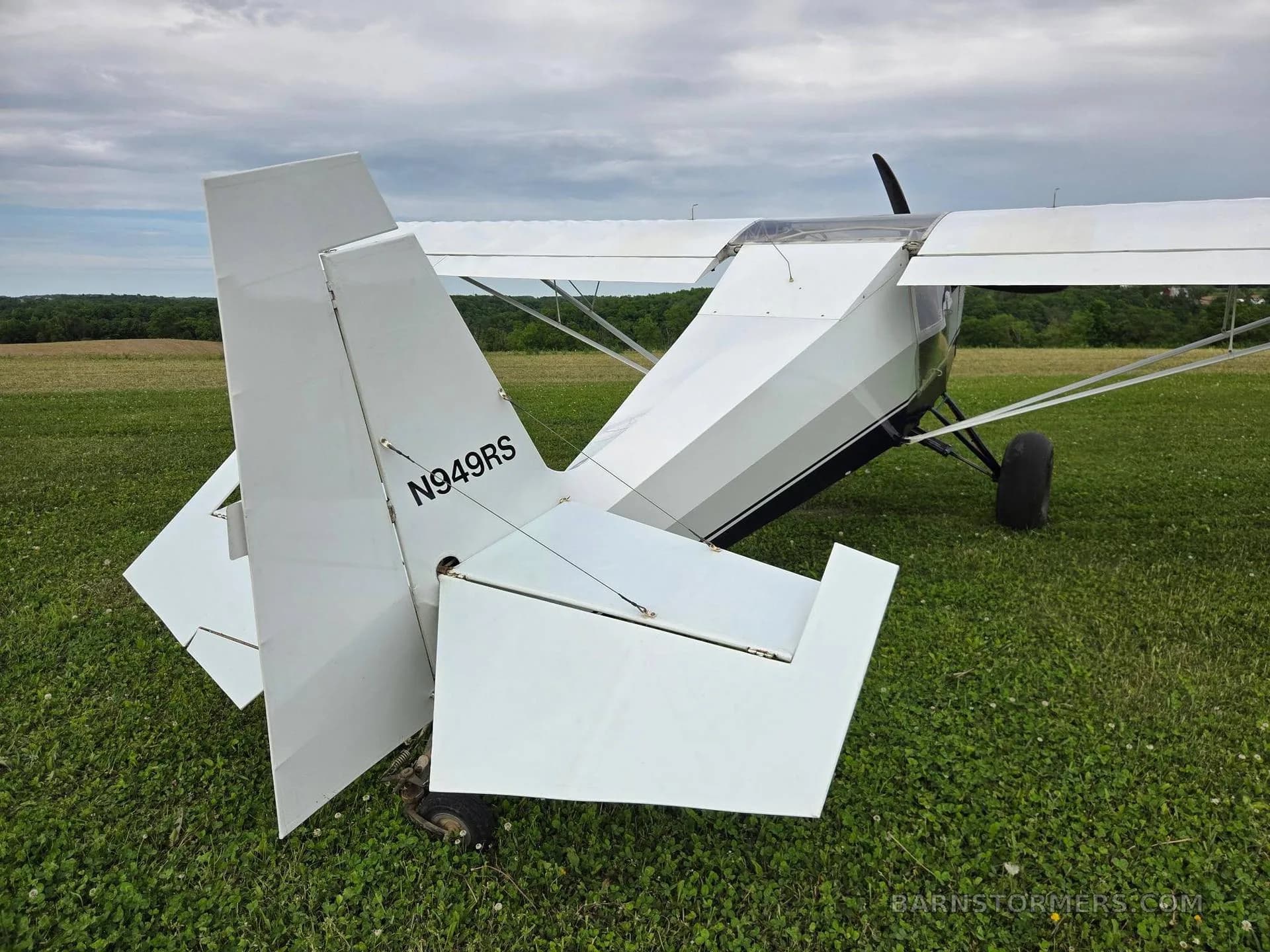 The white tail section of a single-engine aircraft with registration N949RS is shown on a grassy field.