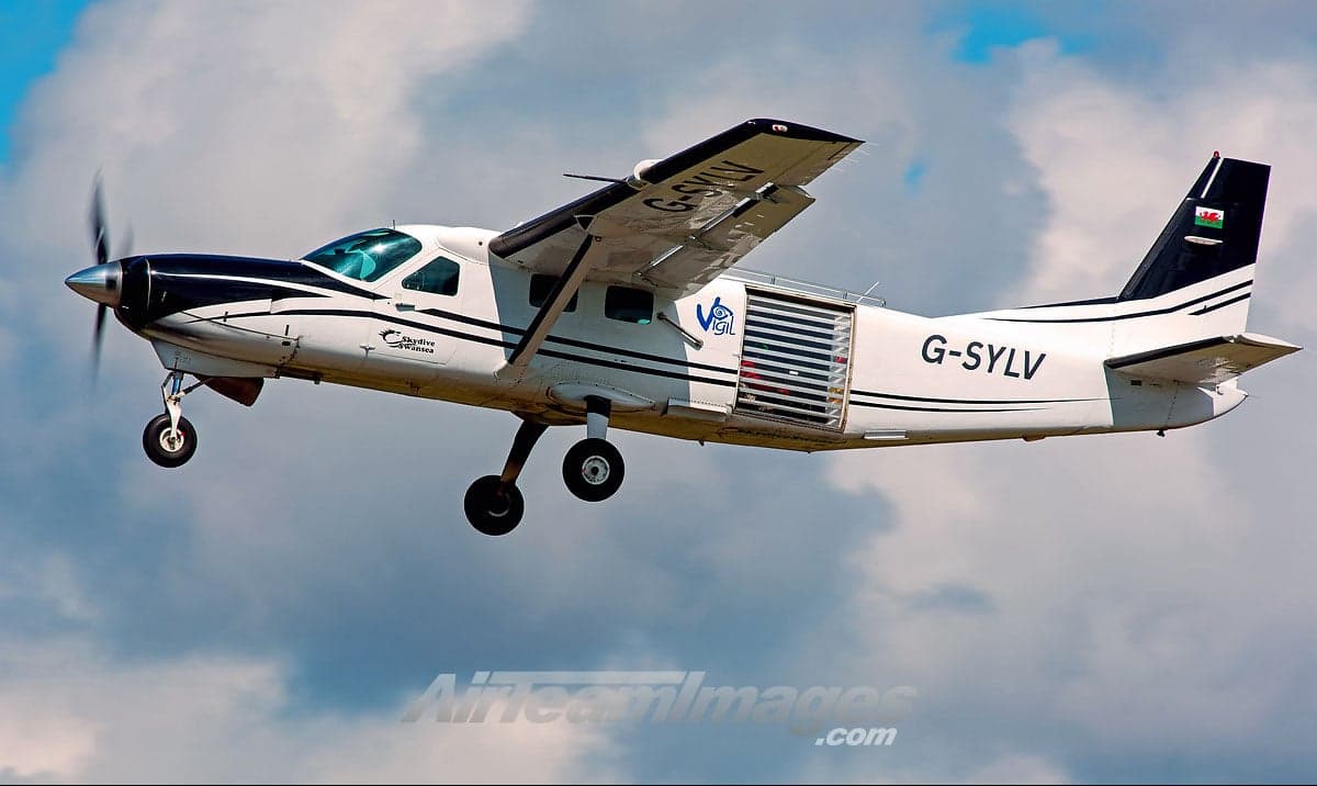Side view of a white and black painted Cessna 208 Caravan in flight.