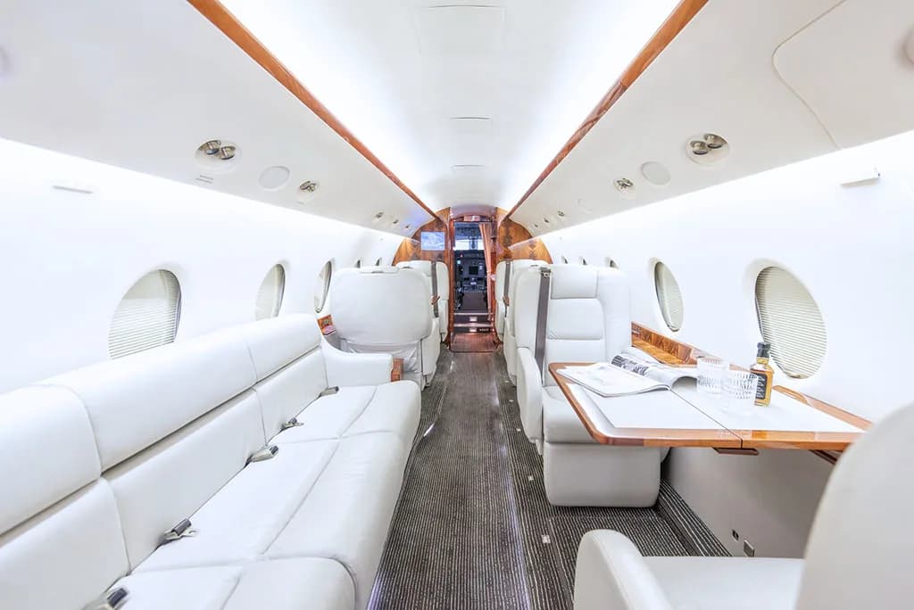 A view of the private jet's cabin with a white leather sofa, individual seats, and a table with drinks.