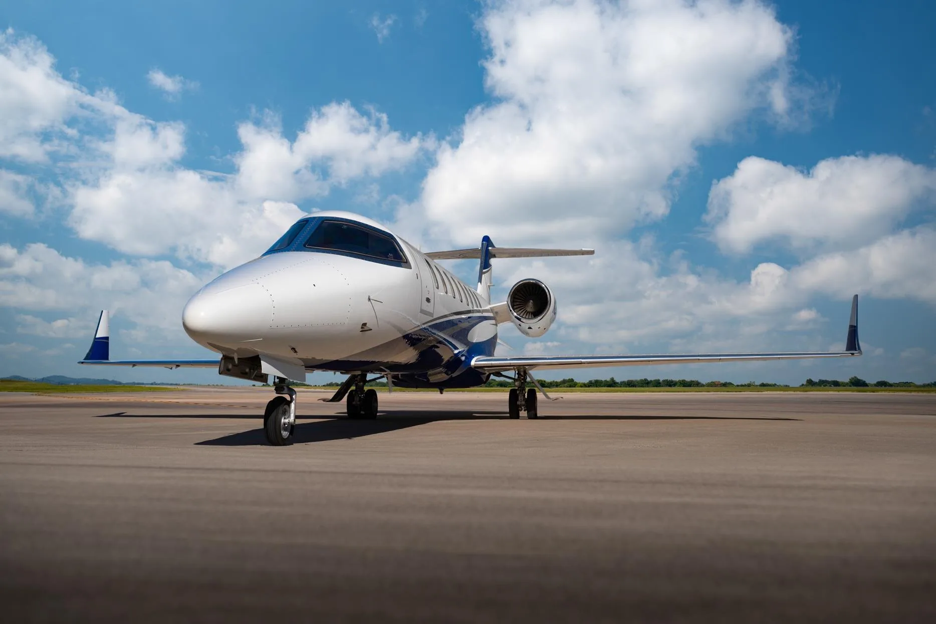 Front three-quarter view of a white and blue Learjet 75 business jet, registration N214TG, on a tarmac.