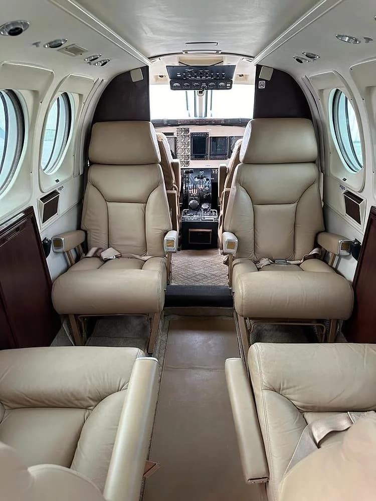 The interior cabin of an aircraft, showing tan leather passenger seats and a view into the cockpit area.