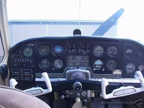 The instrument panel of a small aircraft, featuring various gauges and two white control yokes.
