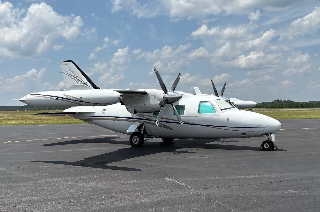 Side view of a white twin-engine aircraft with blue and gold stripes parked on an airfield.