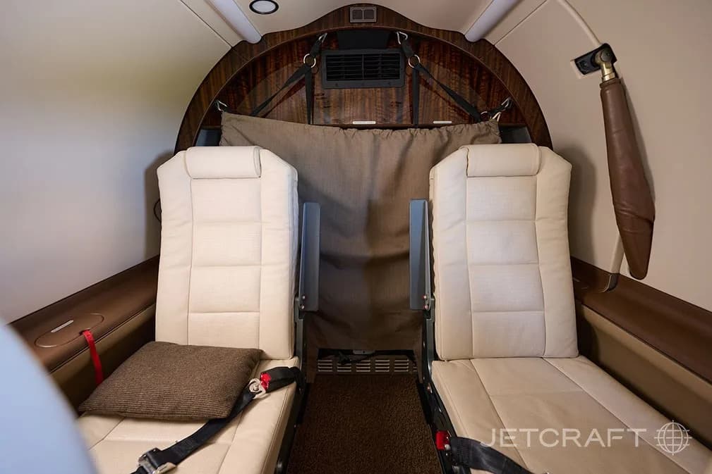 Two light cream leather seats in the rear of the aircraft cabin, with a brown pillow on one seat.