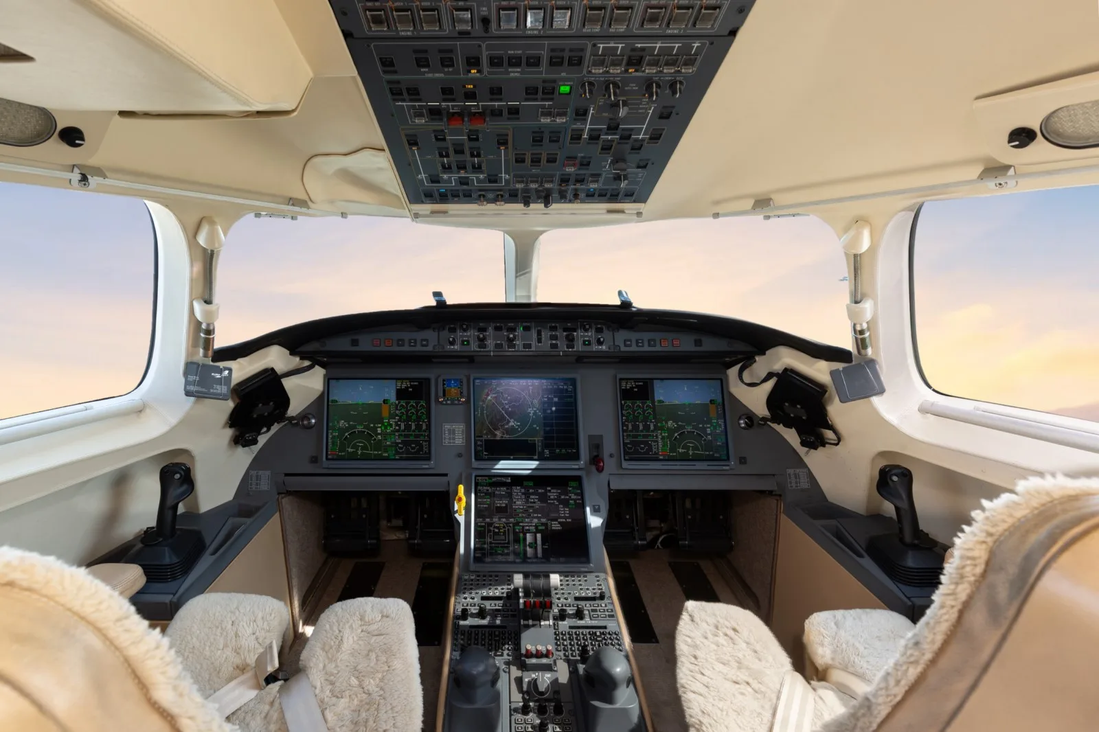 The modern cockpit of a business jet with multiple display screens and an overhead panel.