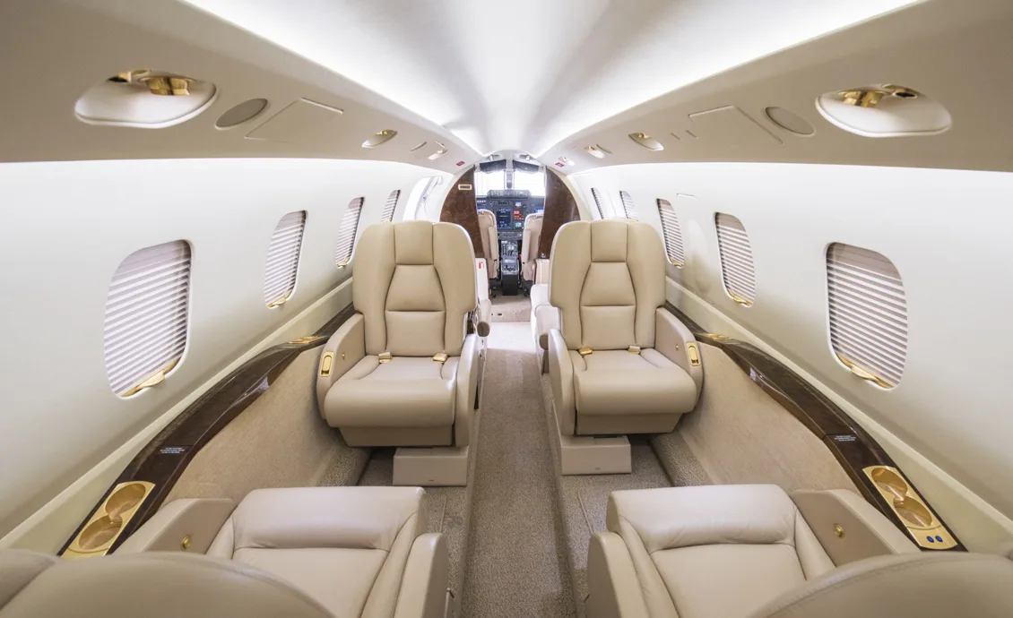 Forward view of the aircraft cabin with tan leather seats and cockpit in the background.