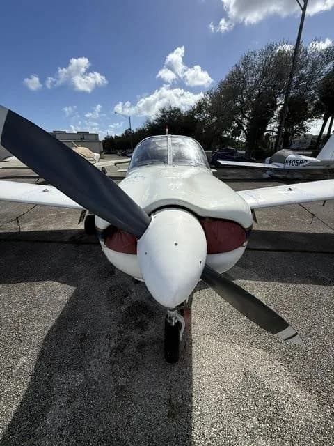 A head-on view of the white Piper Cherokee aircraft, highlighting its propeller and engine cowling.